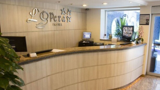 A hotel reception desk with a curved design, a digital screen, and a plant.
