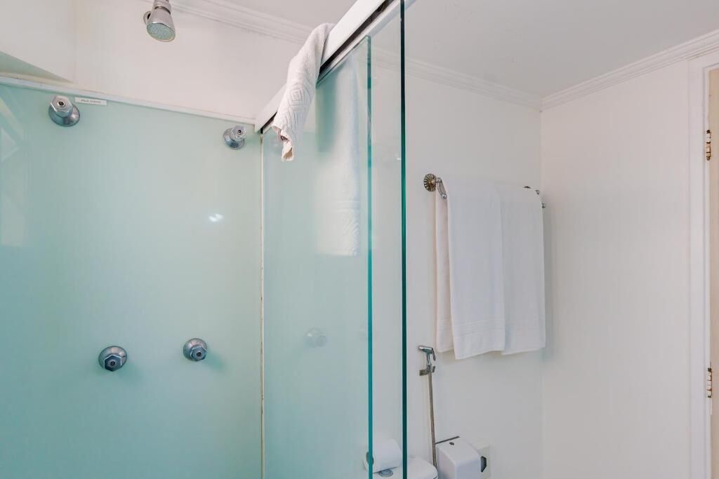 Une douche fermée par des parois de verre, avec une serviette blanche accrochée à la porte.