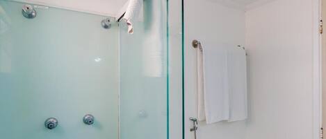 Une douche fermée par des parois de verre, avec une serviette blanche accrochée à la porte.