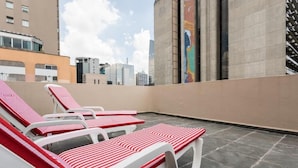 A rooftop terrace with white and red striped lounge chairs, a tiled floor, and a view of surrounding buildings. - Paulista Flat (São Paulo)