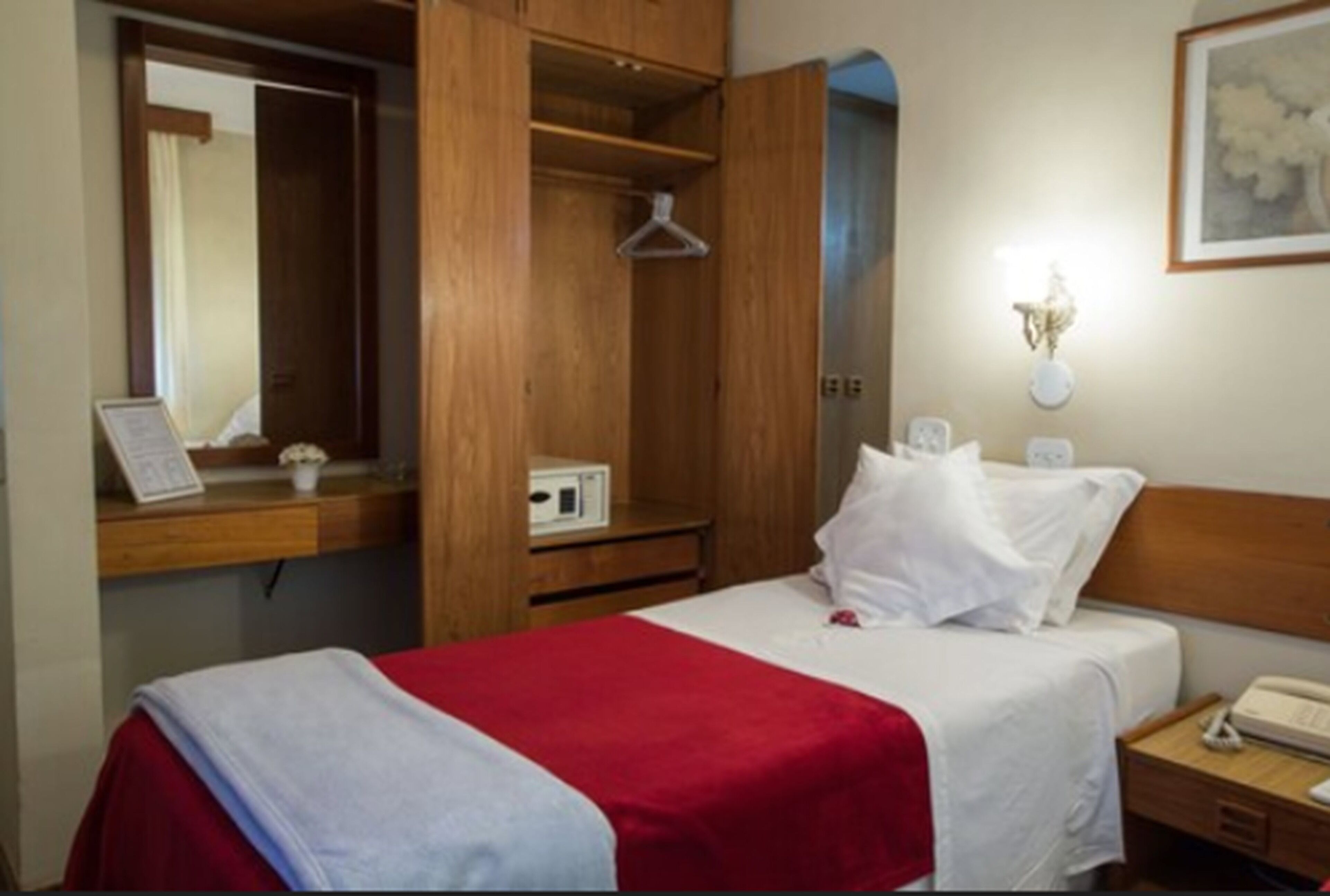 Une chambre d’hôtel comprenant un lit, une armoire en bois, une table de chevet avec une lampe et un téléphone fixé au mur.