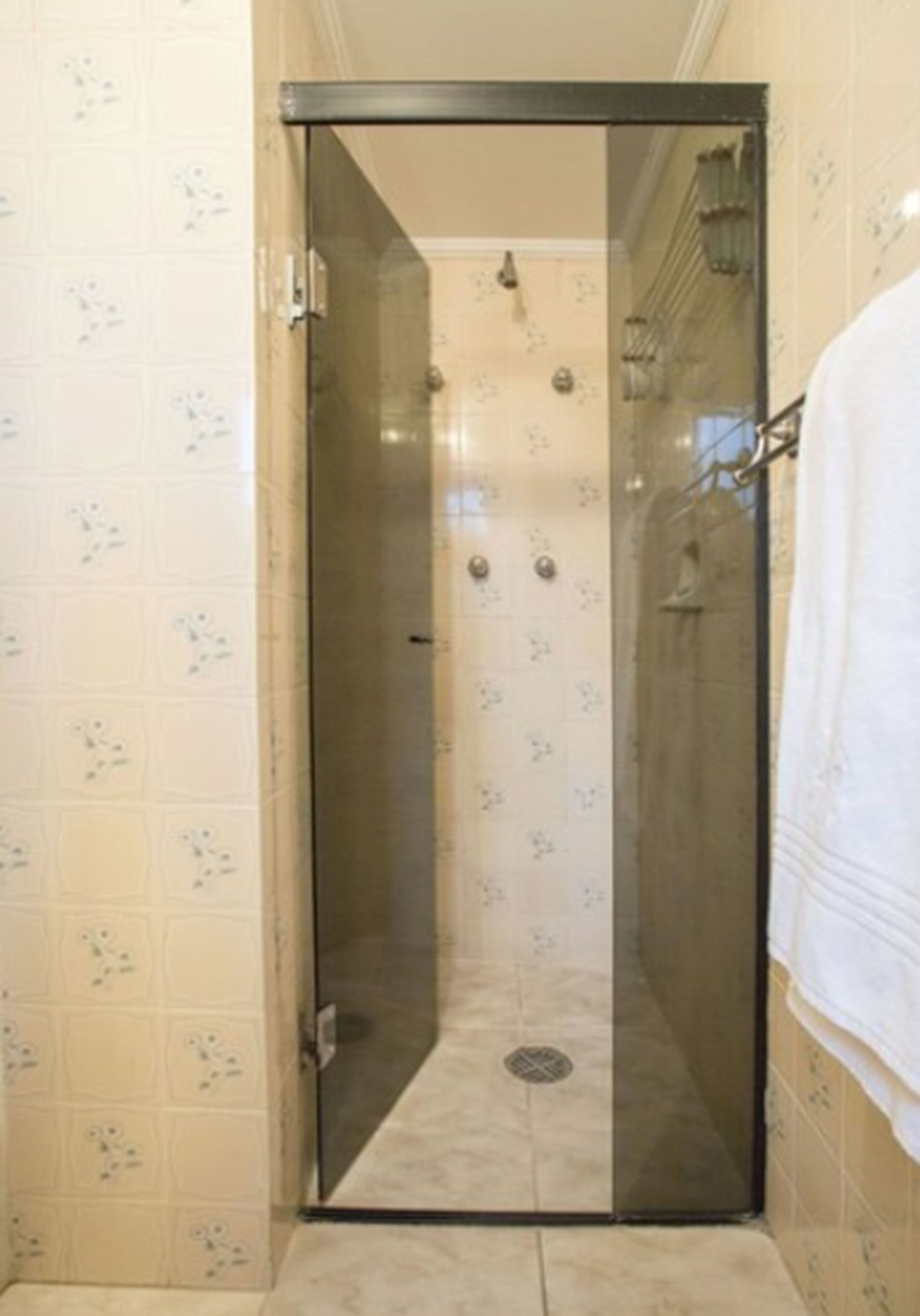 A glass-enclosed shower stall with a tiled wall and a white towel hanging on the right.