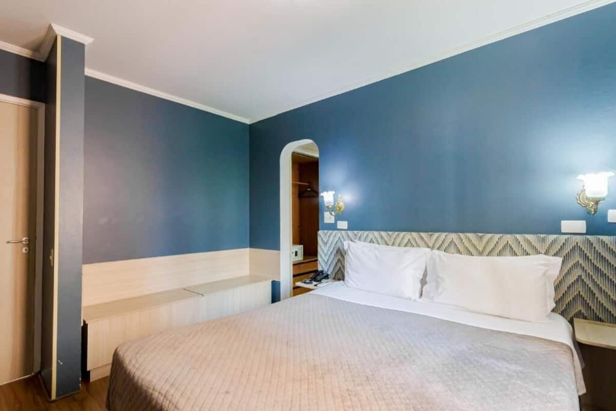 A hotel room with a bed, a nightstand, a mirror, and a wardrobe.