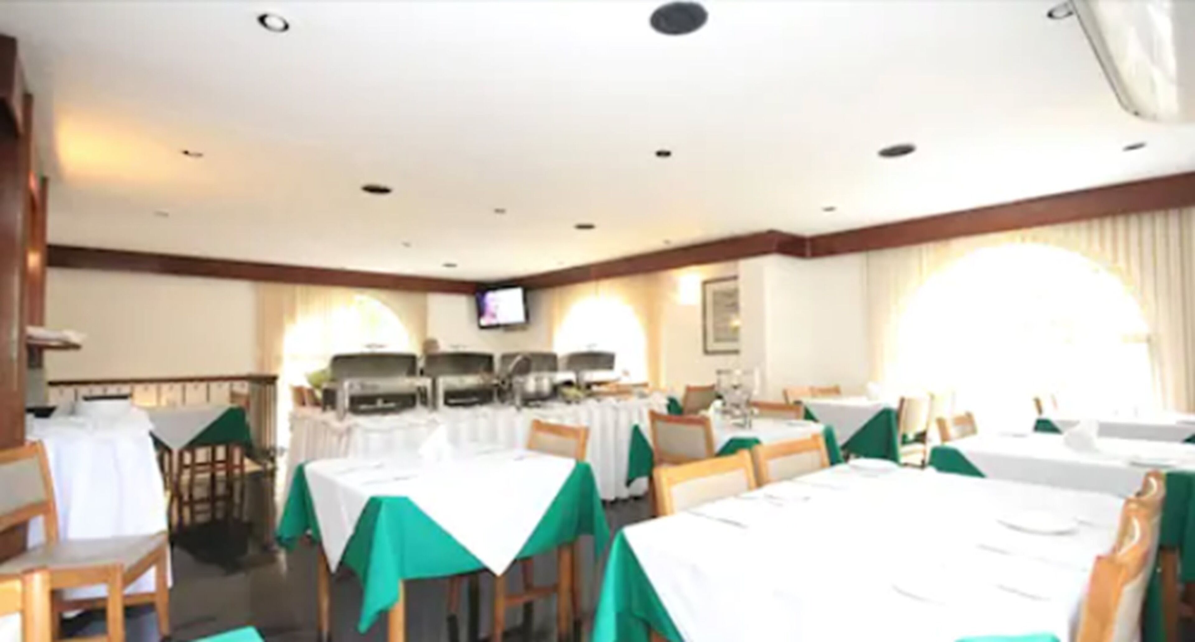 A dining area with multiple tables and chairs, each covered with a white tablecloth and green chair covers.