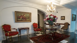 A formal room with a chandelier, red upholstered chairs, a round table with a vase of flowers, and a large framed painting on the wall. - Paulista Flat (São Paulo)