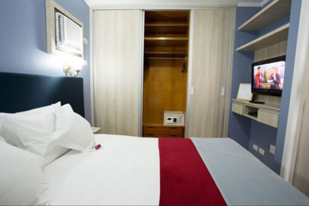 A hotel room with a bed, a television, a closet, and a small table.
