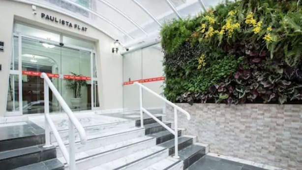 A modern building entrance with marble steps, a glass door, and a vertical garden. - Paulista Flat (São Paulo)