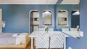 A room with a bed, a dining table with chairs, a kitchen area, and a large mirror. - Paulista Flat (São Paulo)