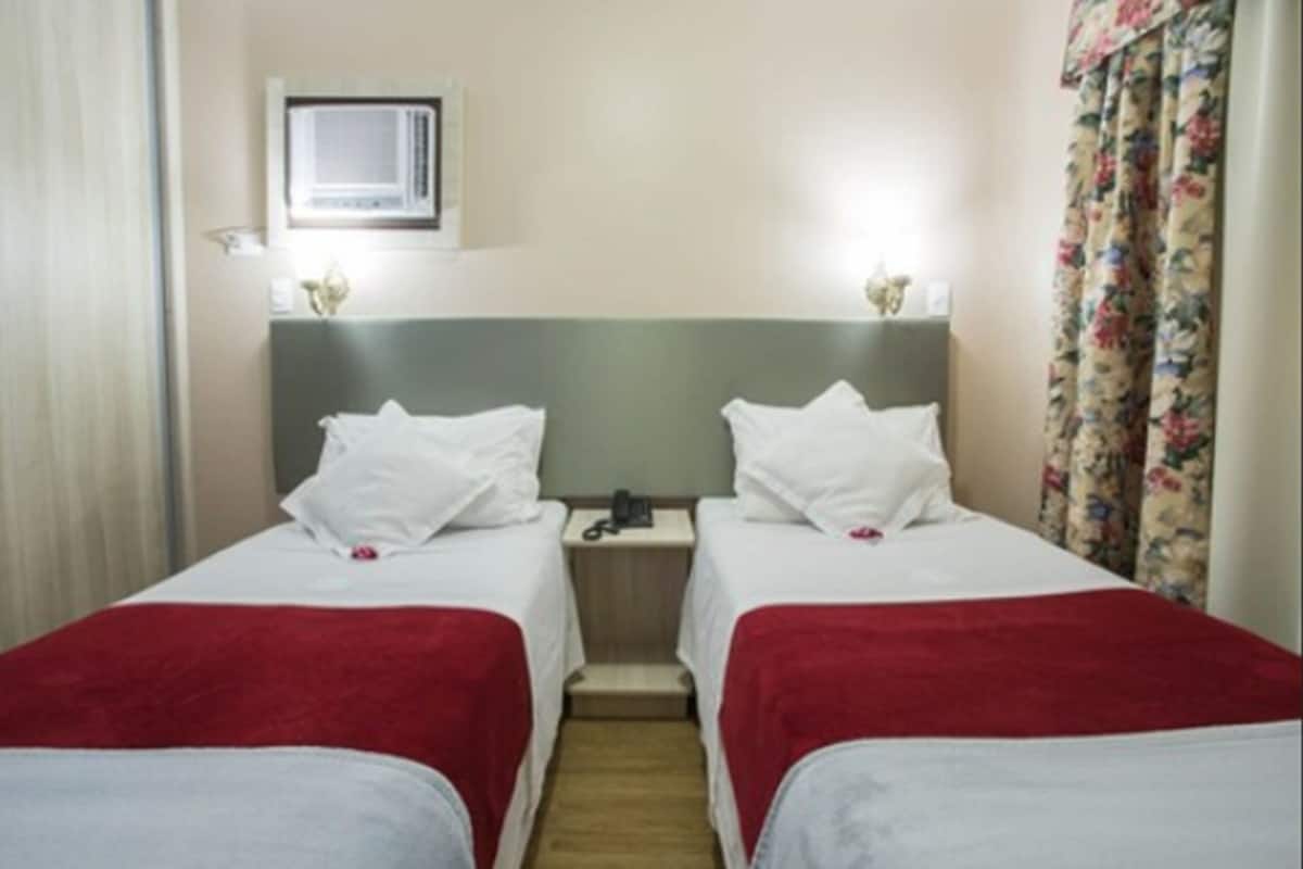 A hotel room with two beds, a nightstand, a telephone, and a window with curtains.