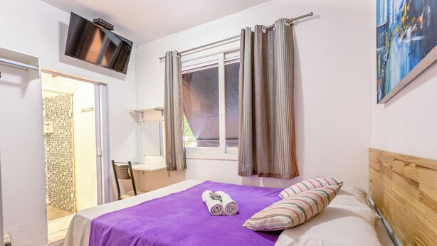 A bedroom with a bed, a TV mounted on the wall, a window with curtains, and a painting on the wall. - Pousada Soft Brooklin (São Paulo)