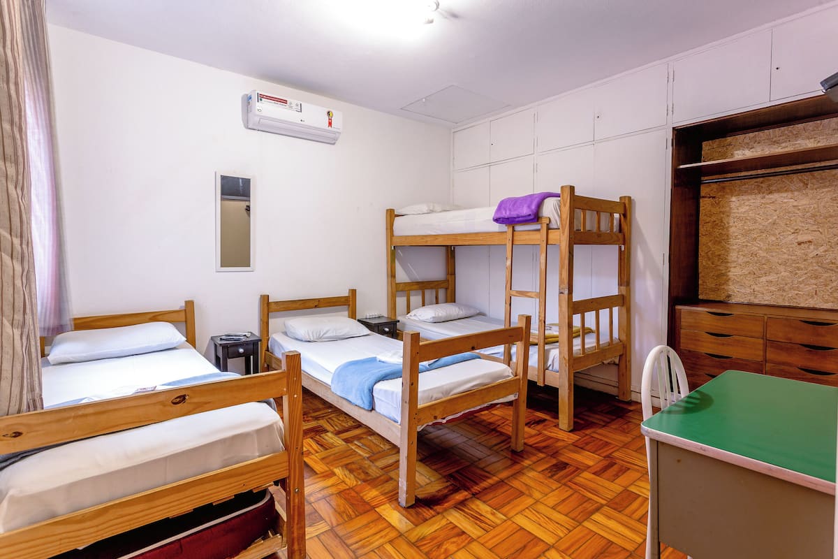 A dormitory room with bunk beds, a small table, a chair, a mirror, and a wardrobe.