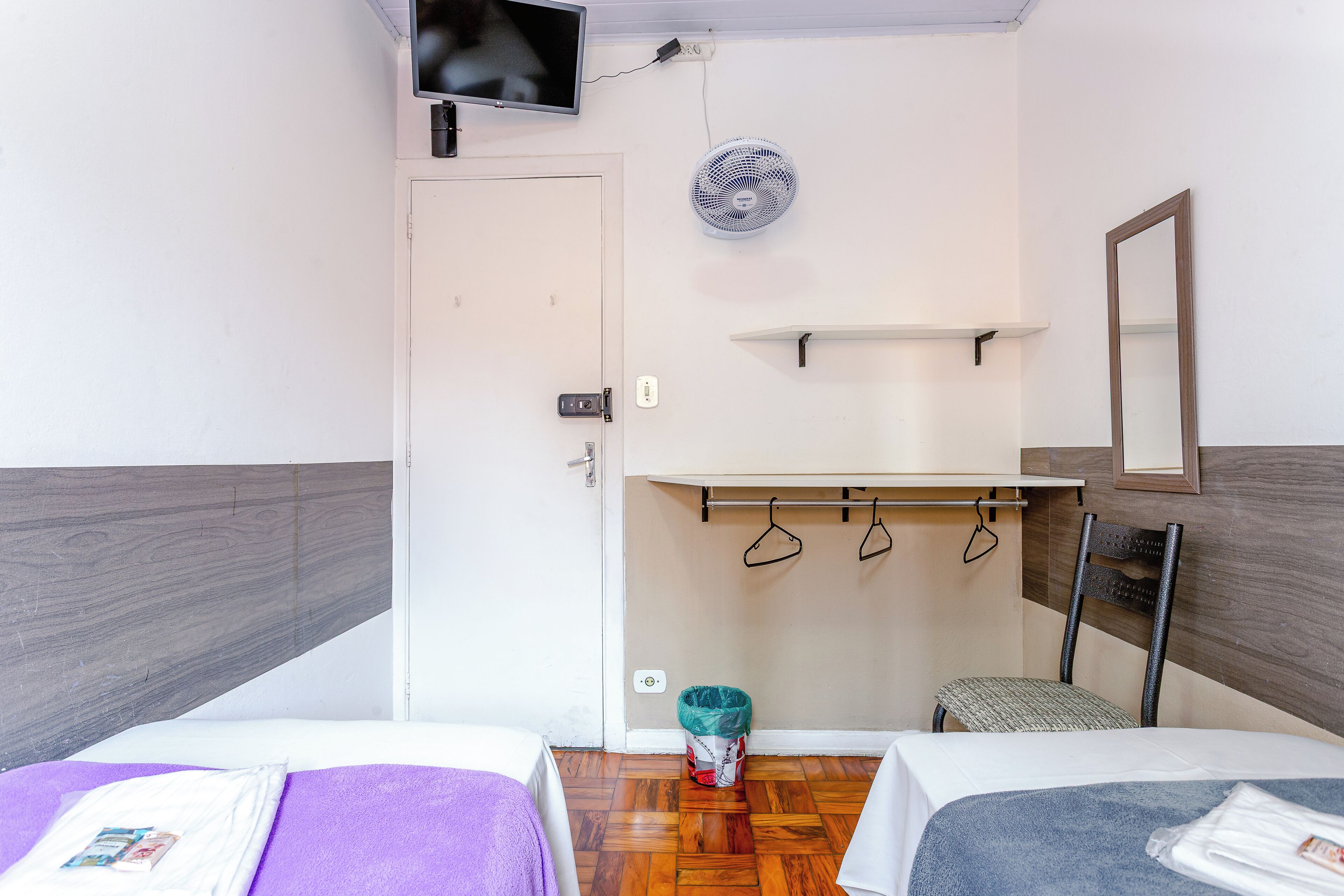 A hotel room with two beds, a television, a fan, a mirror, and a coat rack.