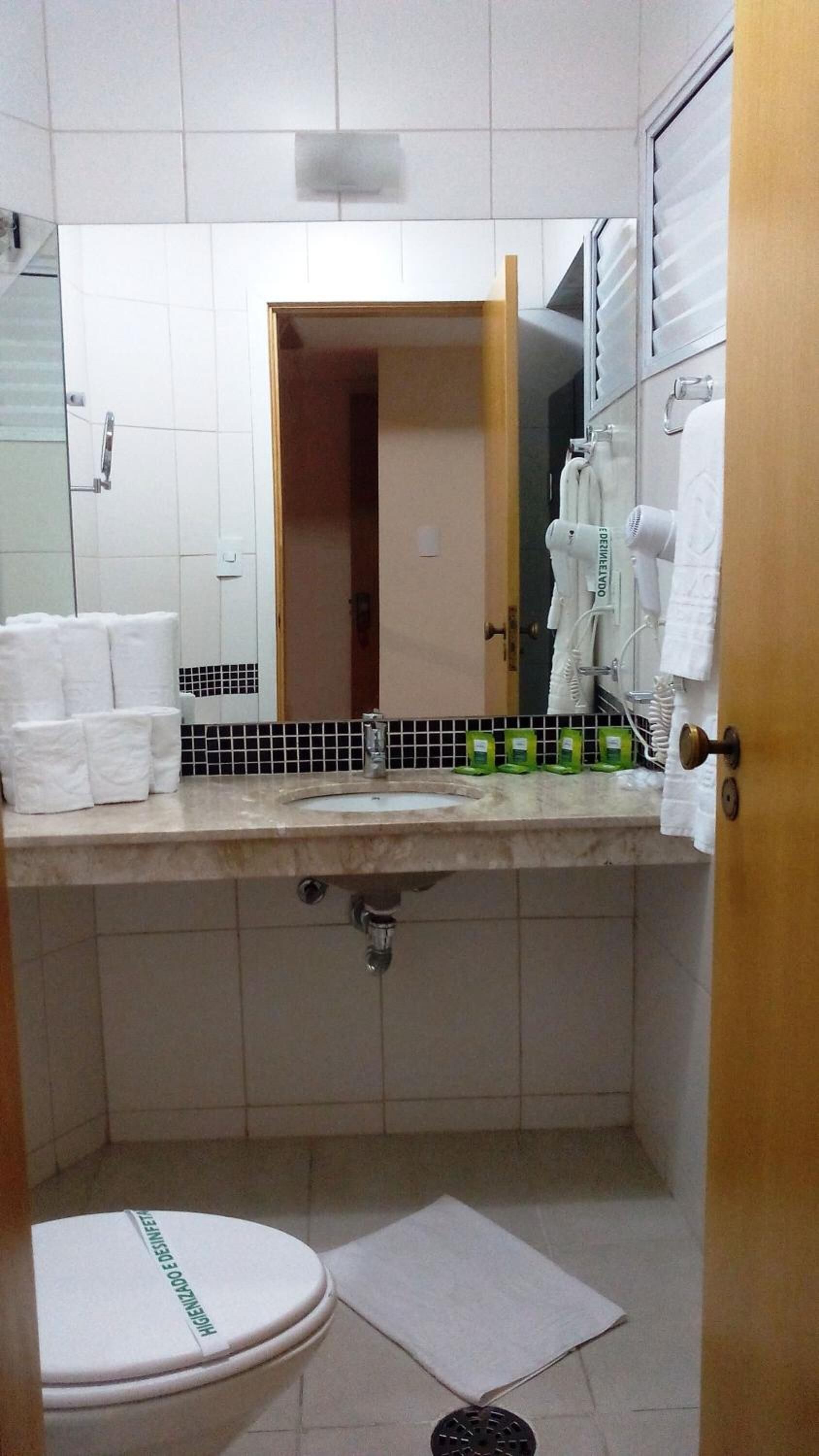 A bathroom with a toilet, sink, and mirror. There are towels and toiletries on the counter.