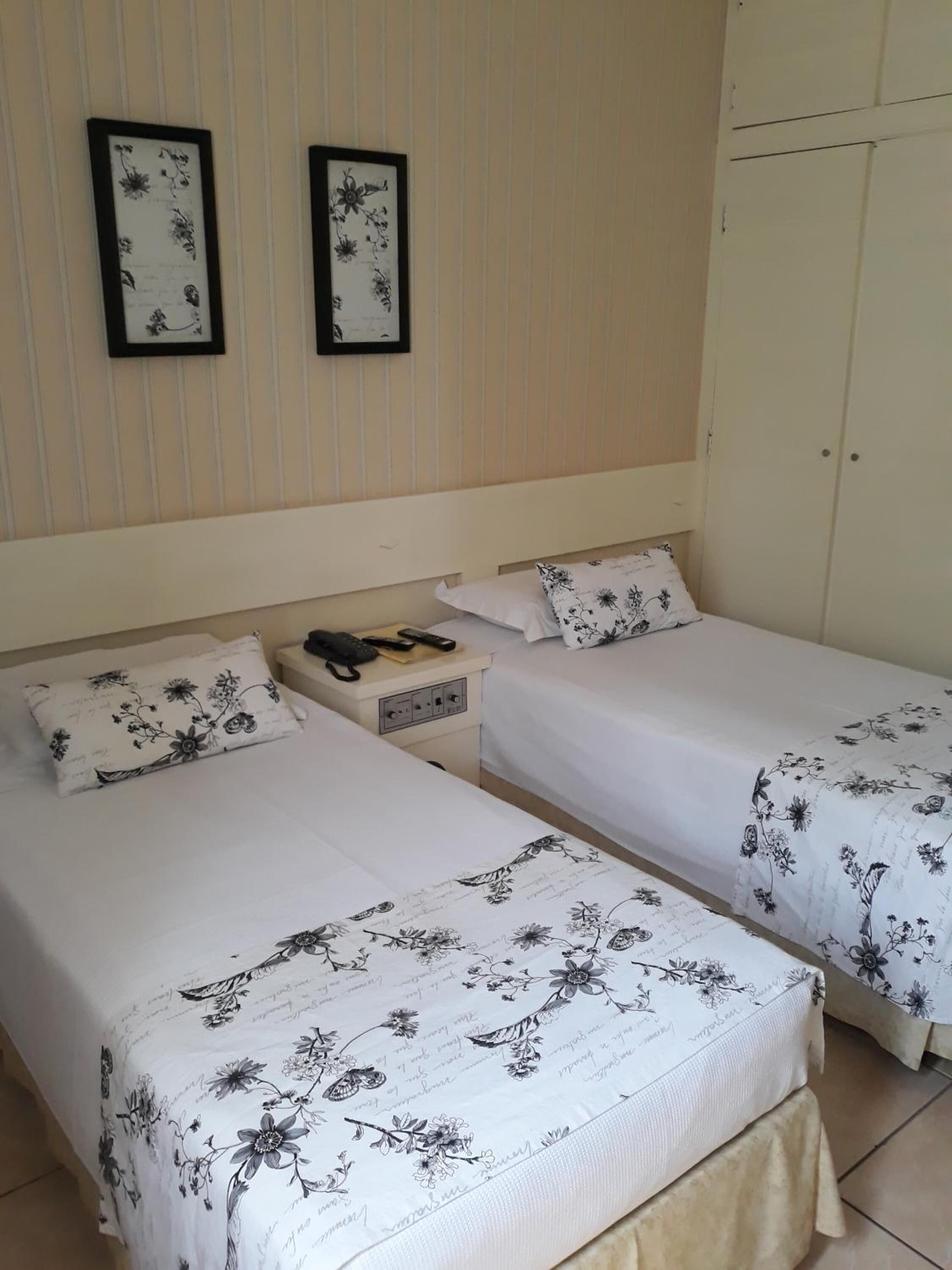Habitación de hotel con dos camas individuales, cada una con ropa de cama de estampado floral. Hay dos cuadros enmarcados en la pared sobre las camas.