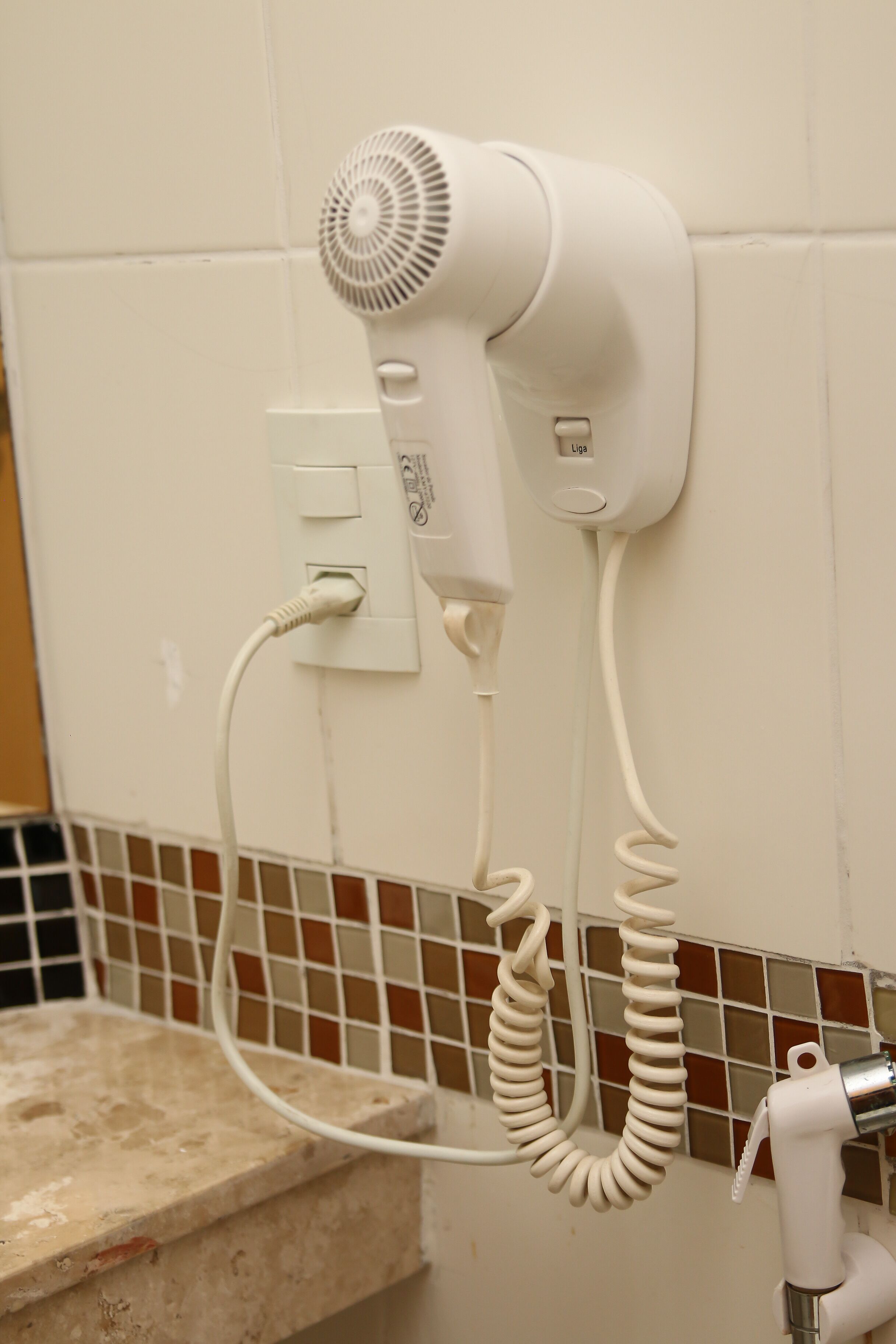 A hair dryer mounted on a wall with a coiled cord.