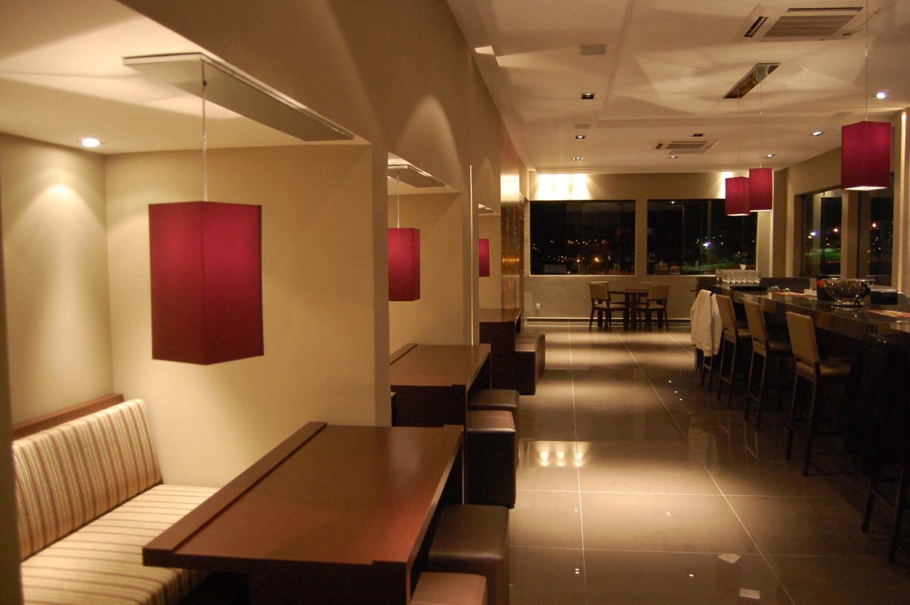 A modern restaurant with high tables and benches, large windows, and red pendant lights.
