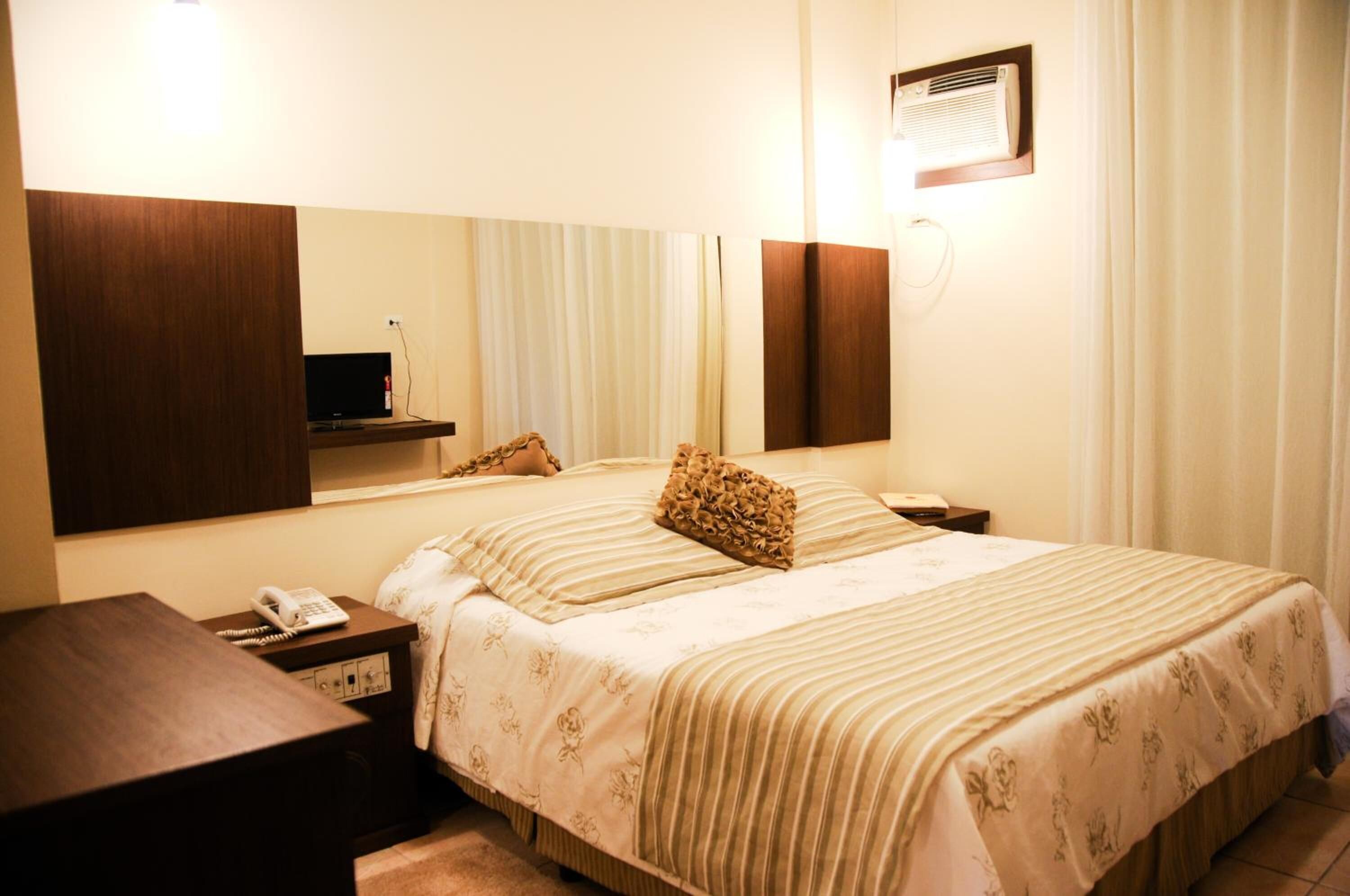 Une chambre d’hôtel avec un grand lit, une table de chevet avec un téléphone, un miroir et un appareil de climatisation fixé au mur.