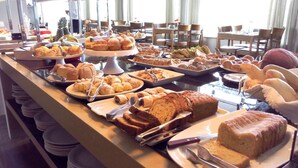 A buffet with various baked goods, including bread, pastries, and a loaf of bread with a glaze. - San Michel Hotel (Taubate)