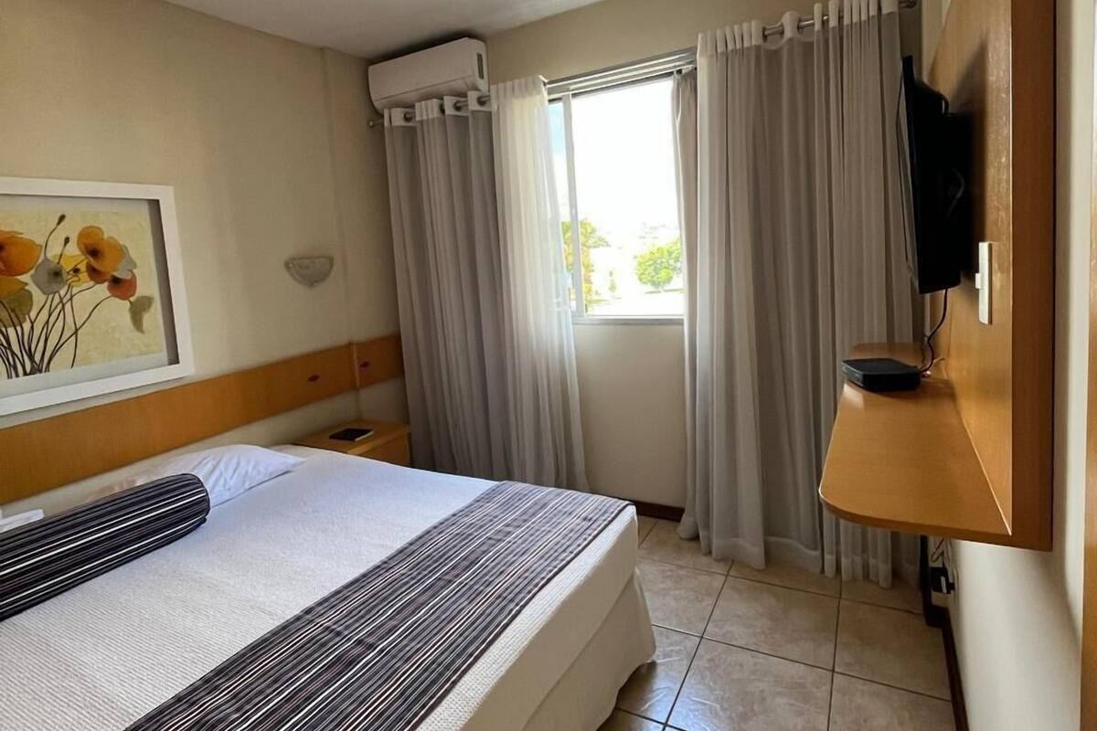 Habitación de hotel con cama, televisión de pantalla plana montada en la pared, ventana con cortinas y aire acondicionado en el techo.