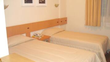 Ett hotellrum med två separata sängar, en sänggavel i trä, ett nattduksbord med en telefon och två inramade tavlor på väggen.