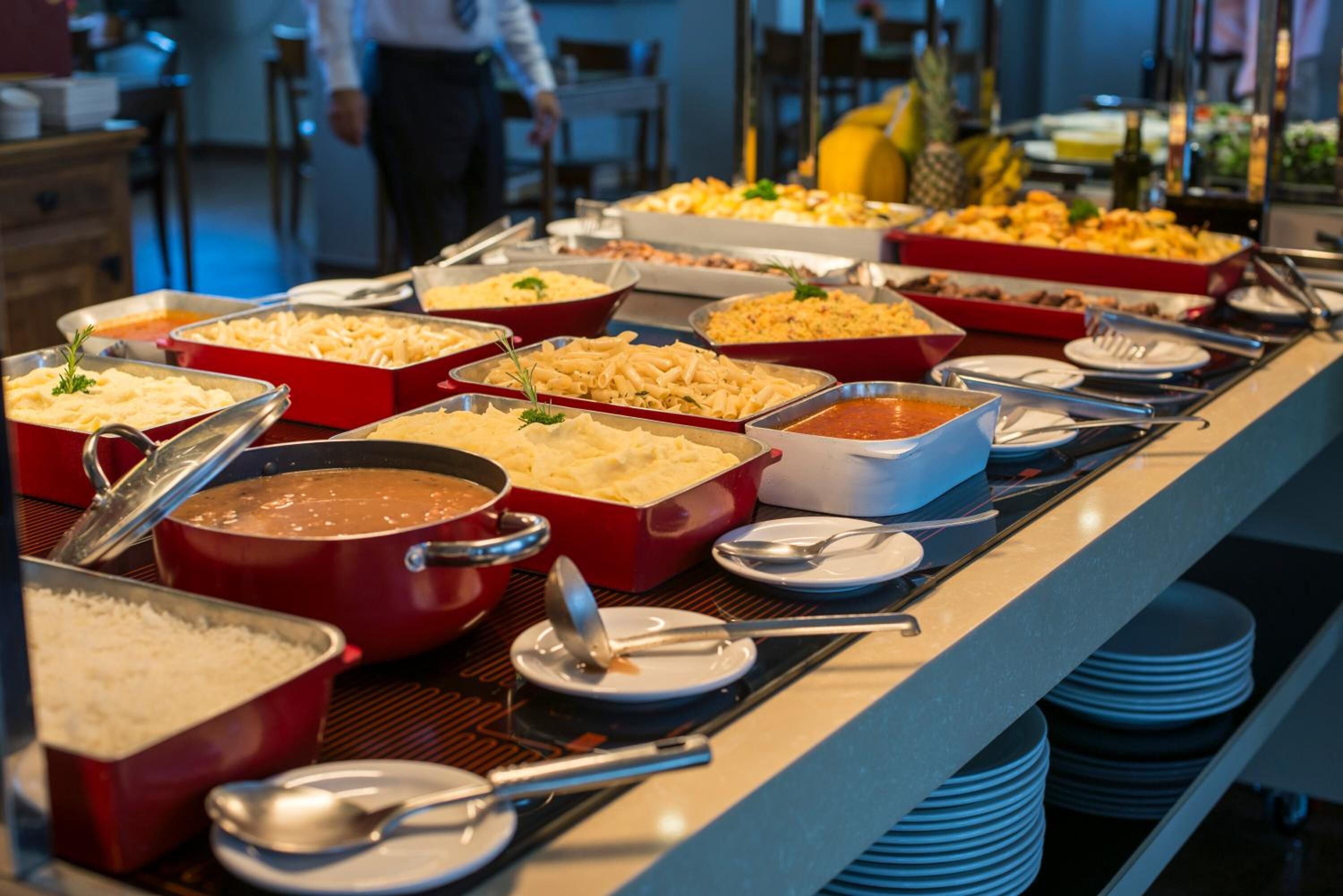 A buffet with various dishes in red and white containers, including pasta, rice, and a soup.