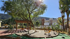 A playground with a wooden structure, green artificial turf, and a brick pathway. - Hotel Zanon (Aguas de Lindoia)