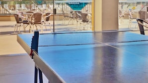 A ping pong table in a room with large windows overlooking a pool area with lounge chairs and umbrellas. - Hotel Zanon (Aguas de Lindoia)