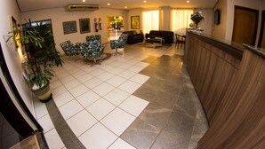 Un hall de hotel con mostrador de recepción, zona de estar con sillas, una mesa de centro y una planta en maceta.