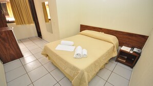 Una habitación de hotel con cama, cabecera de madera, mesita de noche con teléfono y espejo en la pared.