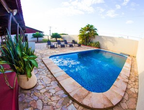 Una piscina con baldosas de piedra, rodeada de sillas de descanso y plantas en macetas.