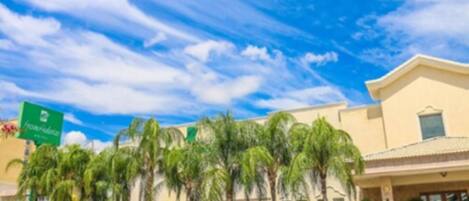A hotel with a signboard, palm trees, and parked cars.