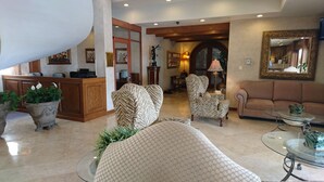 A spacious lobby with a reception desk, patterned armchairs, a sofa, and a glass coffee table. - Hotel Fresno Galerías (Torreón)