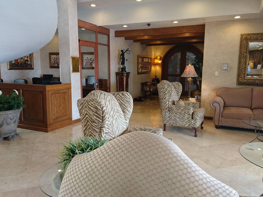 A spacious lobby with a reception desk, patterned armchairs, a sofa, and a glass coffee table.