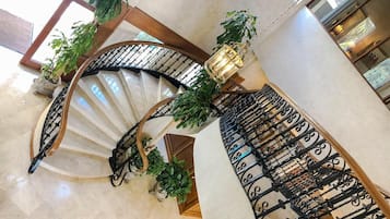 Una gran escalera en espiral con barandillas de hierro forjado negro y detalles de madera, flanqueada por macetas con plantas.