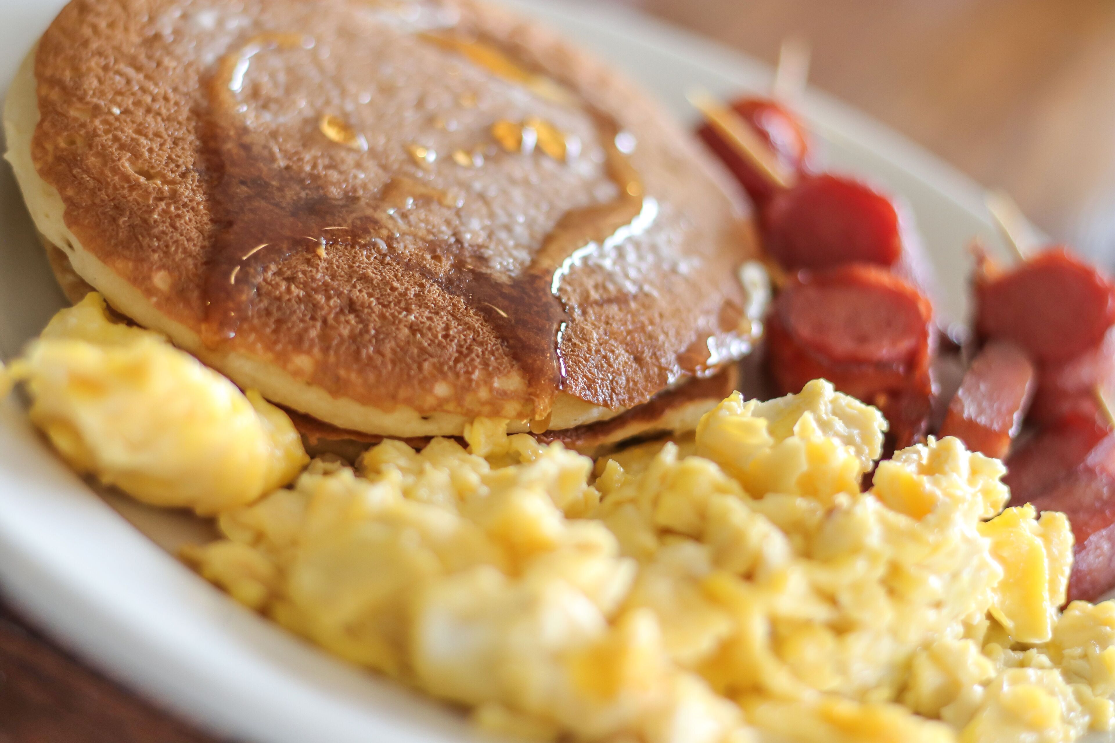 A breakfast plate with pancakes, scrambled eggs, and bacon.
