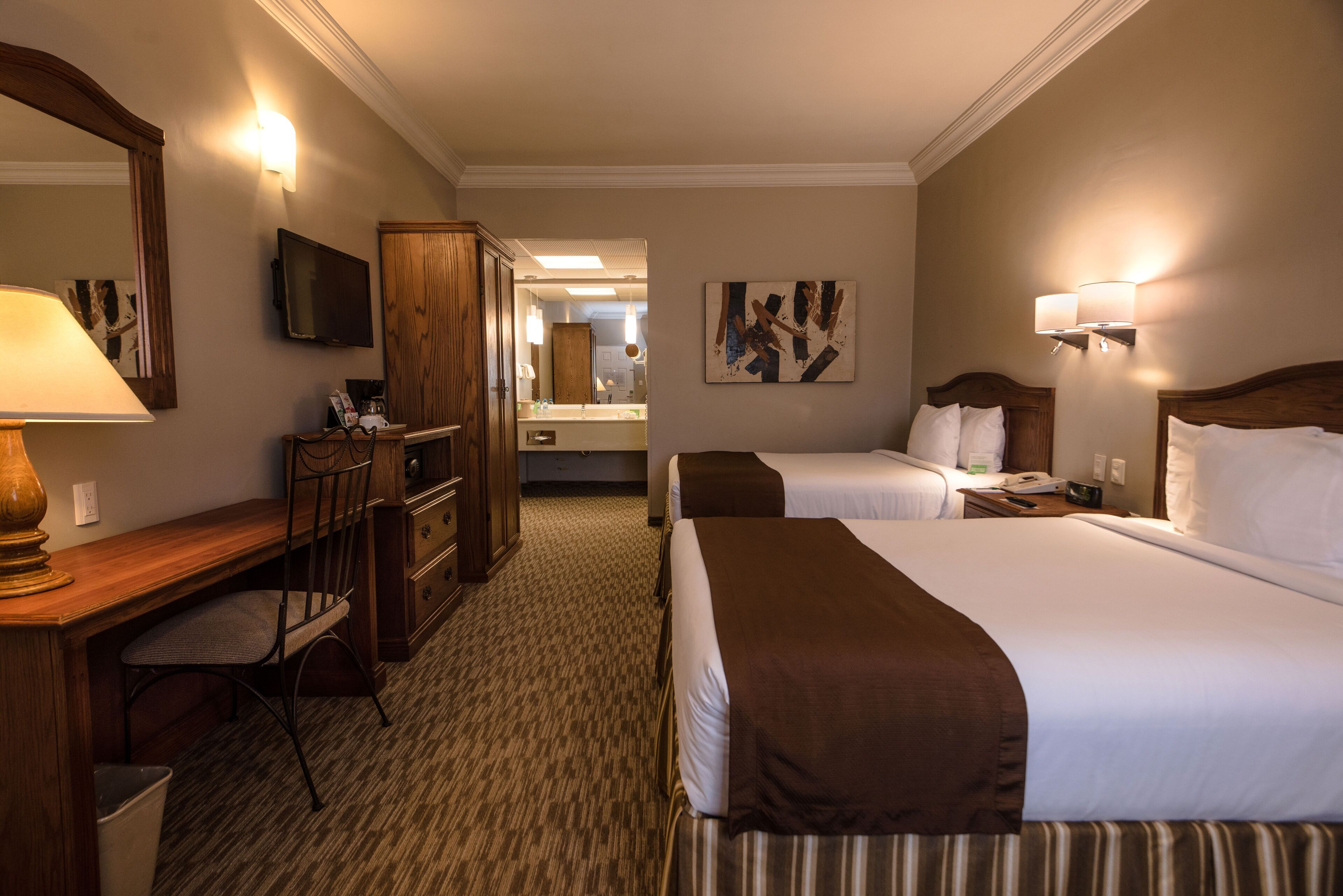 Ein Hotelzimmer mit zwei Betten, einem Schreibtisch, einem Stuhl, einem Fernseher und einem Spiegel.