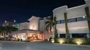 A modern hotel with a well-lit entrance, palm trees, and a clear sky. - Hotel Fresno Galerías (Torreón)