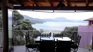 Un espacio al aire libre cubierto con mesa y sillas, con vista a un lago y montañas.