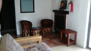 Una sala de estar con un sofá, dos sillas de madera, una mesita de madera y una chimenea.