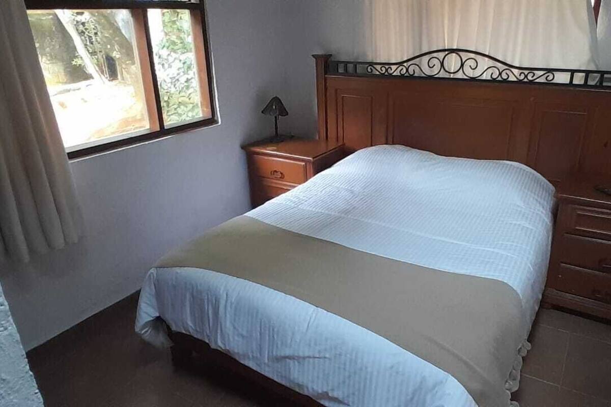 Un dormitorio con cama, mesita de noche, cómoda y ventana con cortinas.