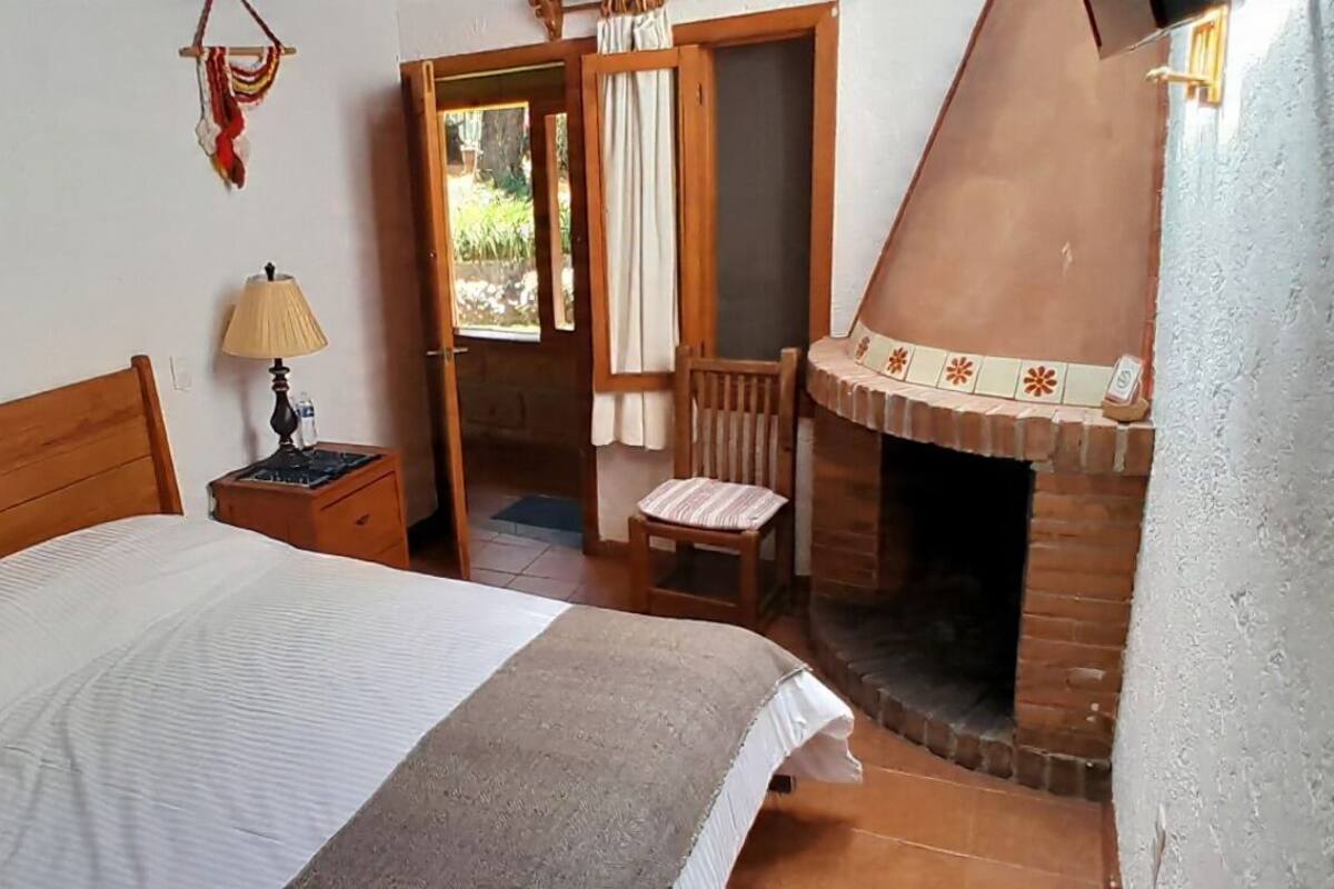 Un dormitorio con una cama, una mesita de noche, una lámpara, una silla y una chimenea.
