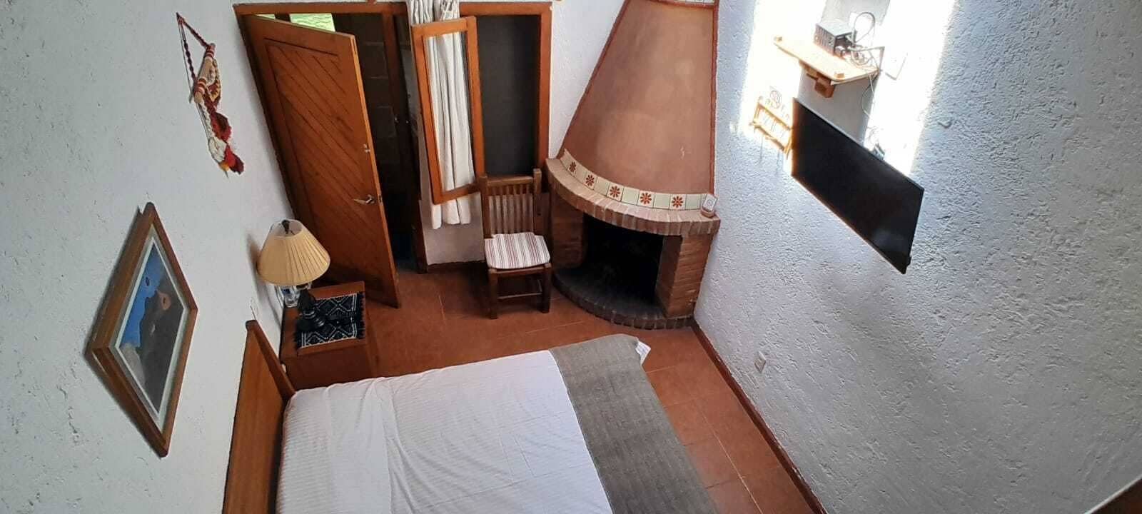 A room with a bed, a chair, a small table with a lamp, a fireplace, and a picture on the wall.