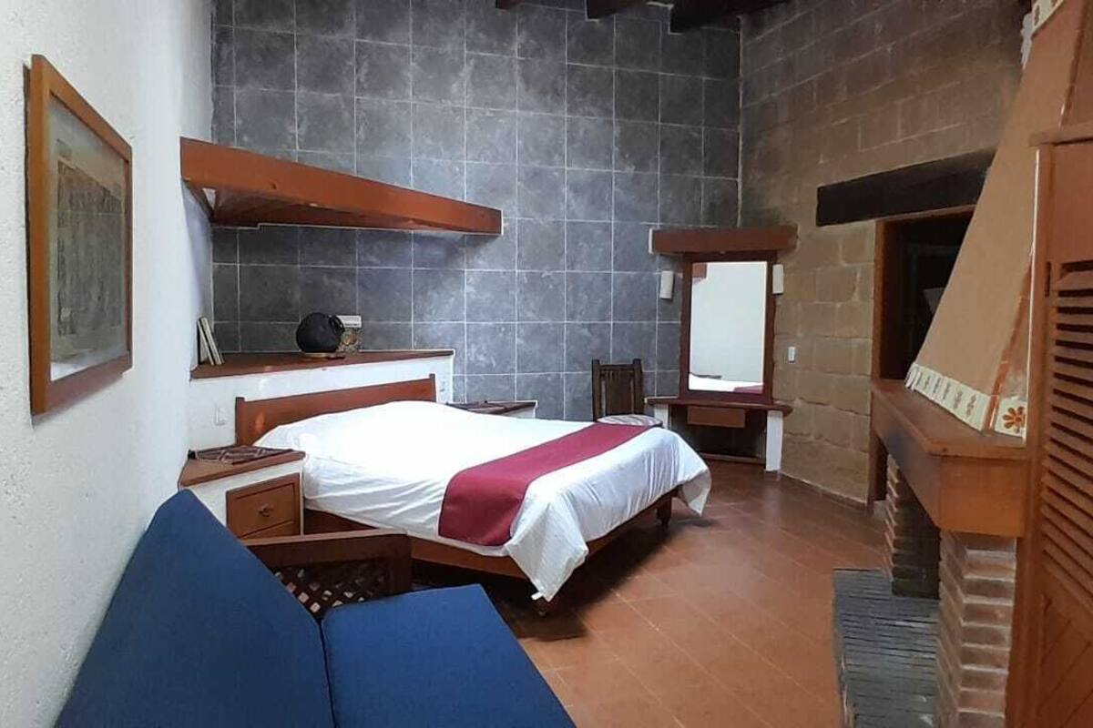 Un dormitorio con una cama, mesitas de noche, un espejo y un banco de madera.