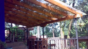 Un patio exterior techado con un pérgola de madera, escalones de piedra y una zona de comedor con sillas y mesas.