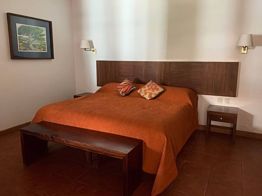 Quarto bem arrumado com uma cama grande, duas almofadas, um banco e duas mesas de cabeceira com abajures.