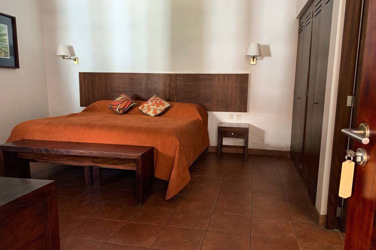 Una habitación de hotel con una cama de madera, dos mesitas de noche, un banco y un armario.