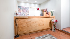 Un espace d’accueil avec un comptoir en bois, une peinture abstraite aux couleurs vives, un logo et un vase décoratif orné de fleurs.