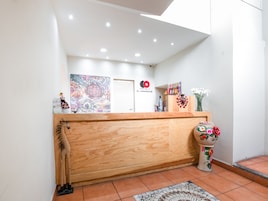 Un área de recepción con mostrador de madera, un cuadro abstracto de colores, un logotipo y un jarrón decorativo con flores.