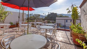 Une terrasse extérieure avec des tables et des chaises, un parasol rouge et des plantes en pot.