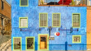 Un immeuble de deux étages avec une façade bleue, des encadrements de fenêtres verts et un parapluie rouge sur le toit.